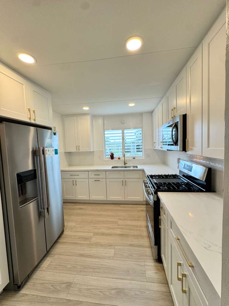 Bright white galley kitchen with gas range and marble waterfall counter — O'ahu