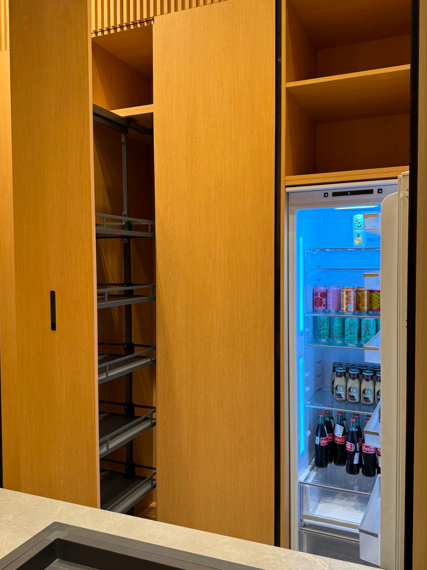 Custom oak walk-in pantry with pull-out wire shelving and glass-door beverage refrigerator on display at Ward Design Center Kapolei