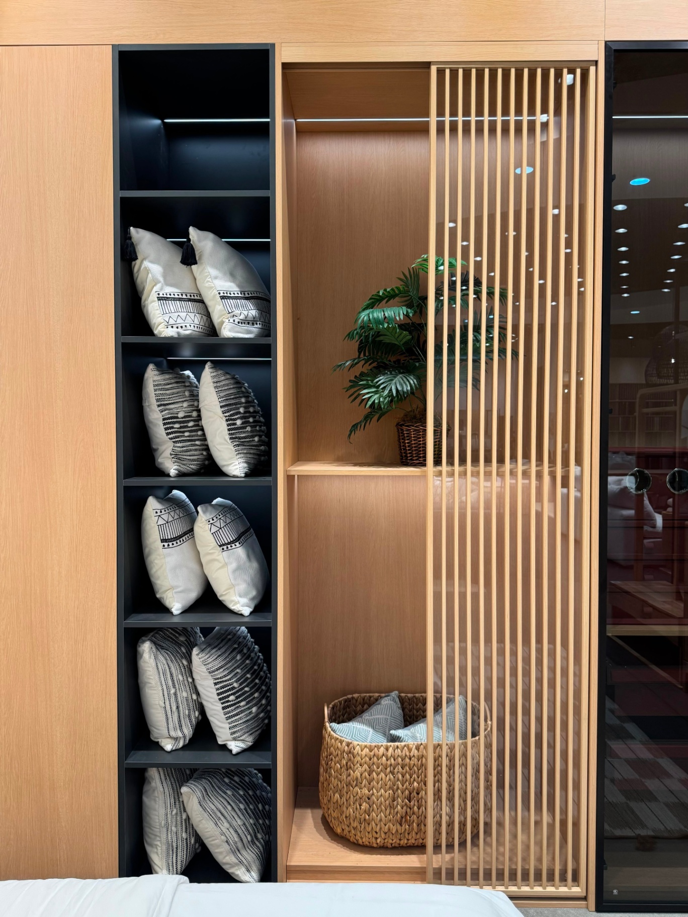 Custom bedroom wardrobe display with black open shelving, vertical oak slat divider, and warm LED lighting — Ward Design Center showroom Oahu
