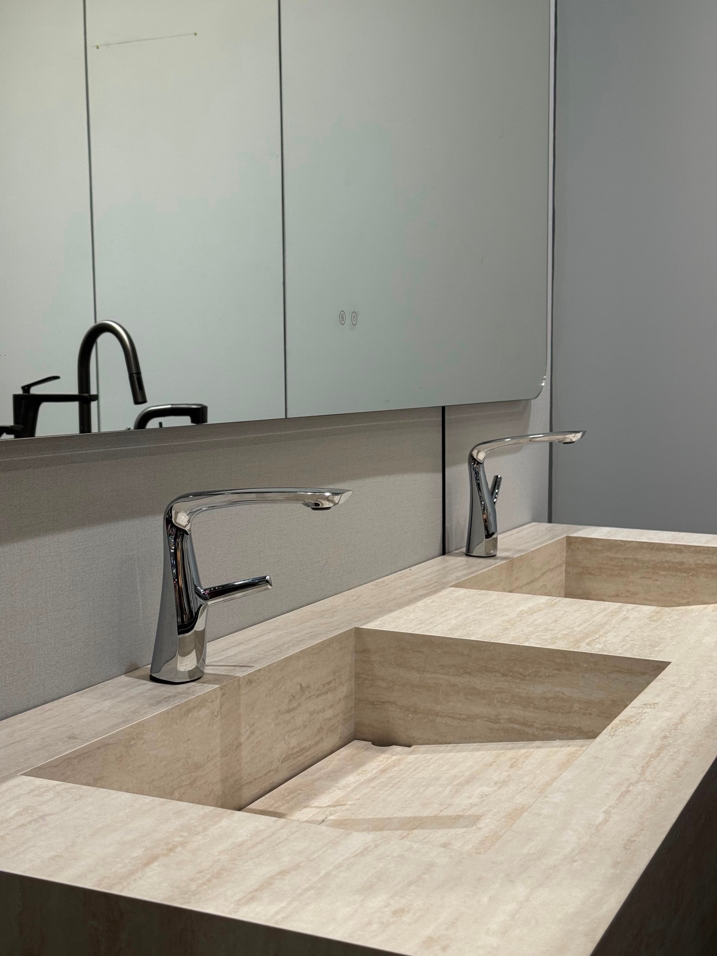 Carved travertine double vanity with integrated sloped sink basins and chrome modern faucets — Ward Design Center bathroom showroom Kapolei