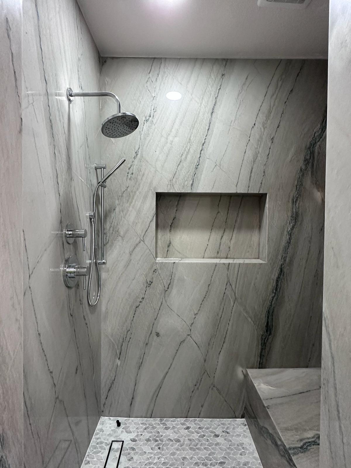 Walk-in shower with book-matched quartzite slab walls and pebble mosaic floor — O'ahu