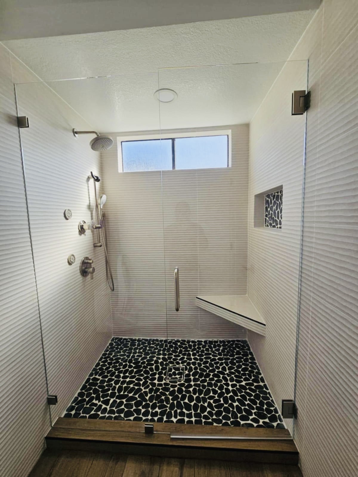 Walk-in shower with textured white tile, pebble mosaic floor and frameless glass — O'ahu