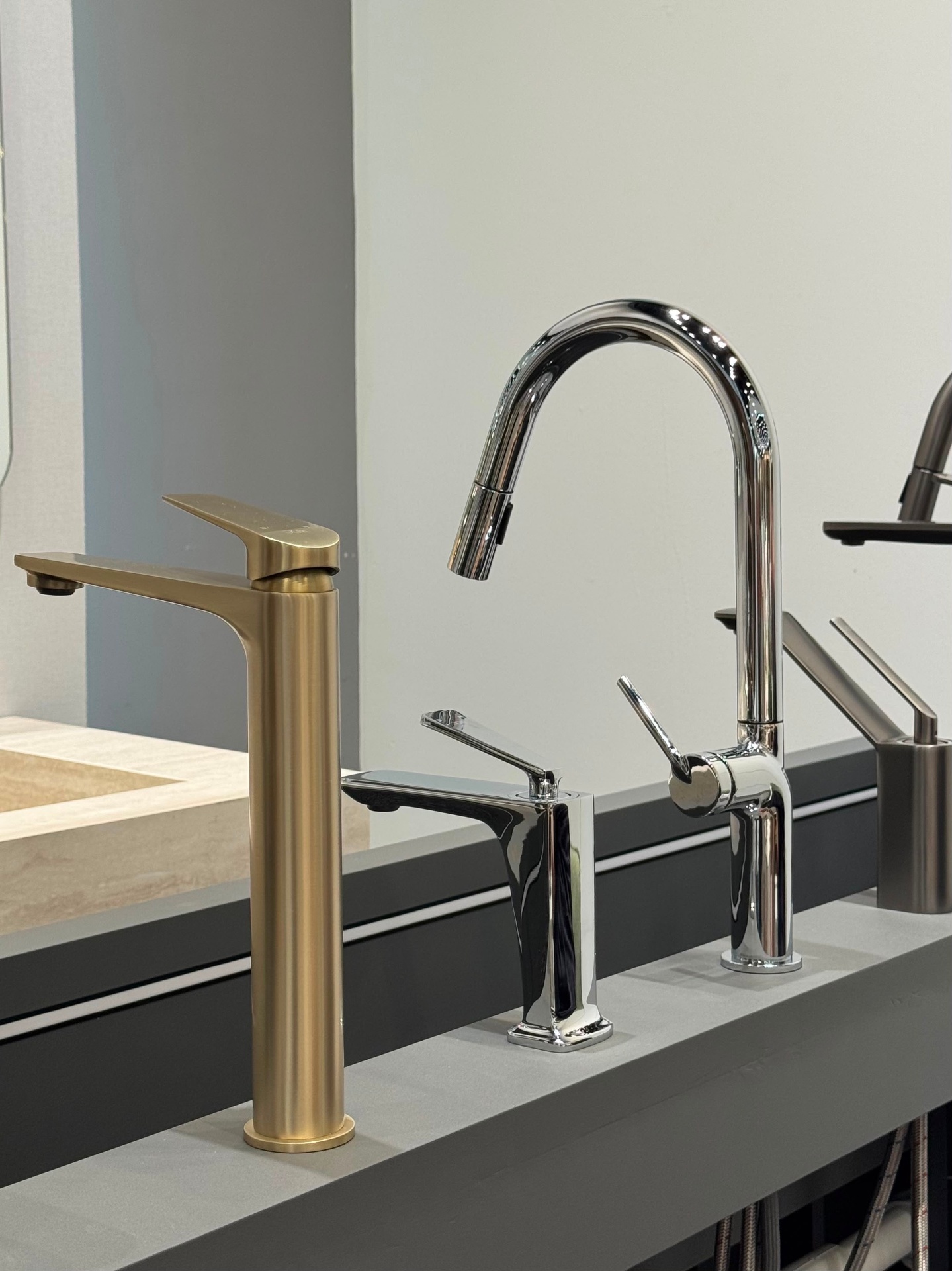Three bathroom and kitchen faucets in brushed brass, polished chrome and gunmetal finishes displayed on a stone countertop at Ward Design Center Oahu showroom