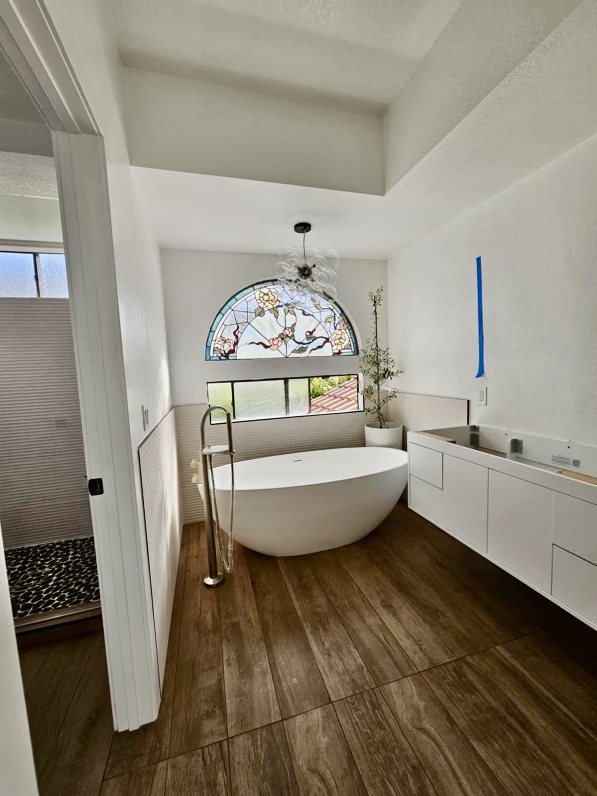 Freestanding tub beneath stained-glass arched window with wood-look tile flooring — O'ahu