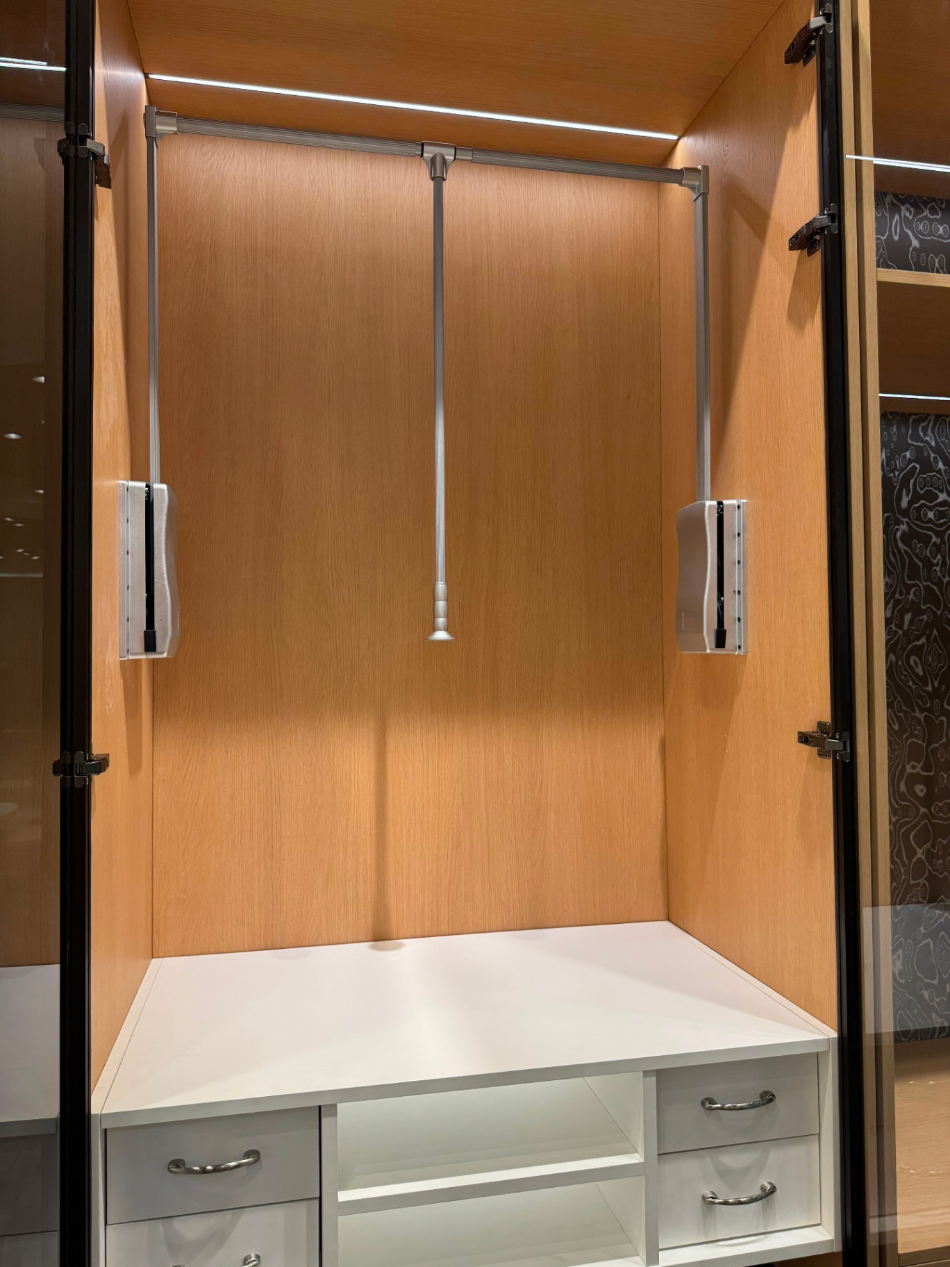Wardrobe interior with pull-down closet rod hardware and integrated LED lighting on display at Ward Design Center Oahu showroom